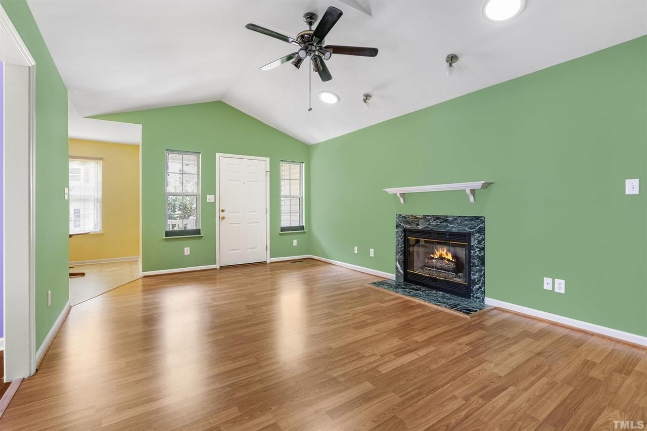 A large open living room with wood floor, bright green walls, central fireplace, white trim